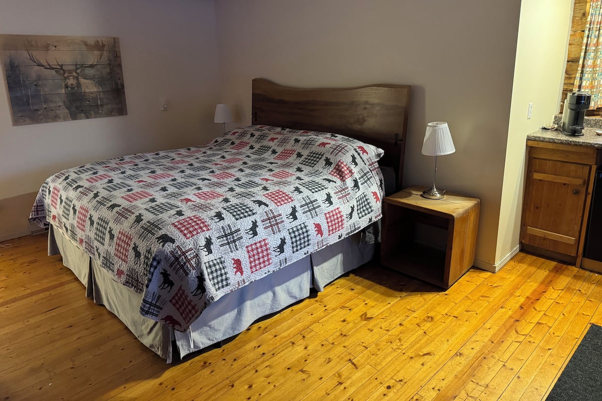 Quarto com cama de madeira, mesa de cabeceira com abajur, cómoda de madeira e colcha com estampas de animais.