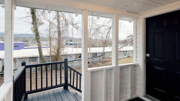 En inglasad veranda med en svart dörr, vita räcken och utsikt över ett bostadsområde med träd och byggnader.
