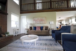 A spacious living room with a high ceiling, a fireplace, a dining area, and a kitchen visible through an open door. - Serenity with Mountain Views 3BR Deckside Views (Greeneville)
