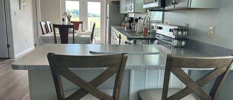 A modern kitchen with a central island, wooden chairs, and a dining area with a view.