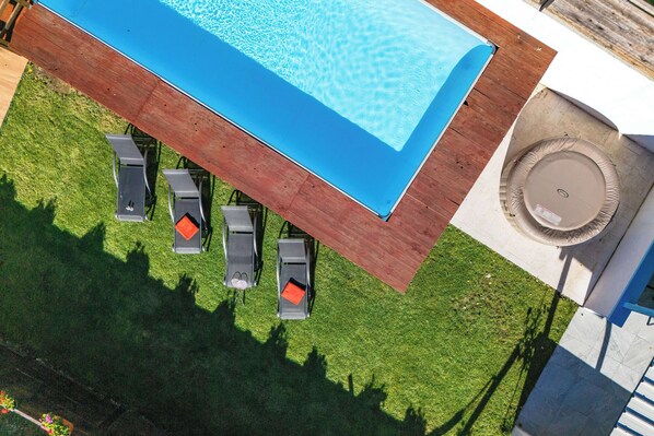 Eine Vogelperspektive auf einen Swimmingpool mit einer Holzterrasse, umgeben von einem gepflegten Rasen und einigen Liegestühlen.