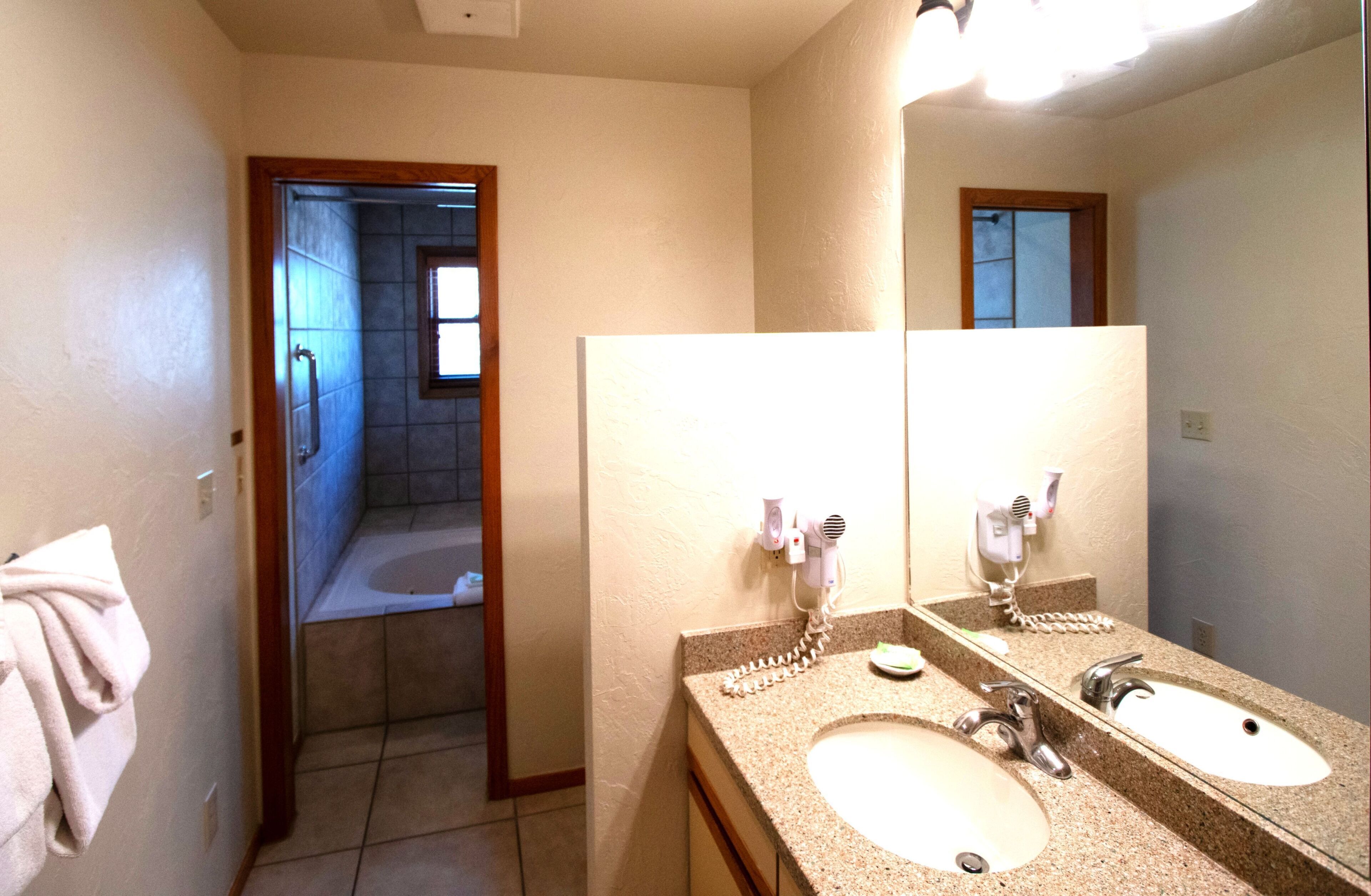 A bathroom with two sinks, a large mirror, and a shower area visible through an open door.