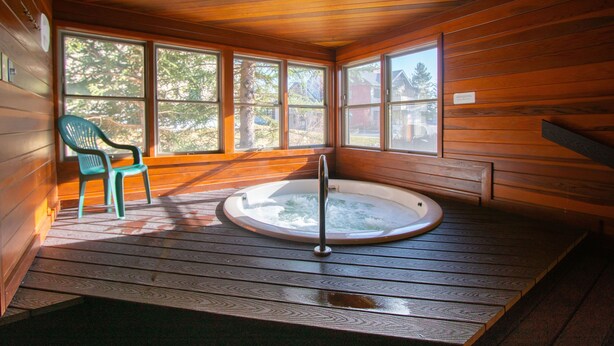 Une cabane en bois avec un jacuzzi, une chaise et de grandes fenêtres.