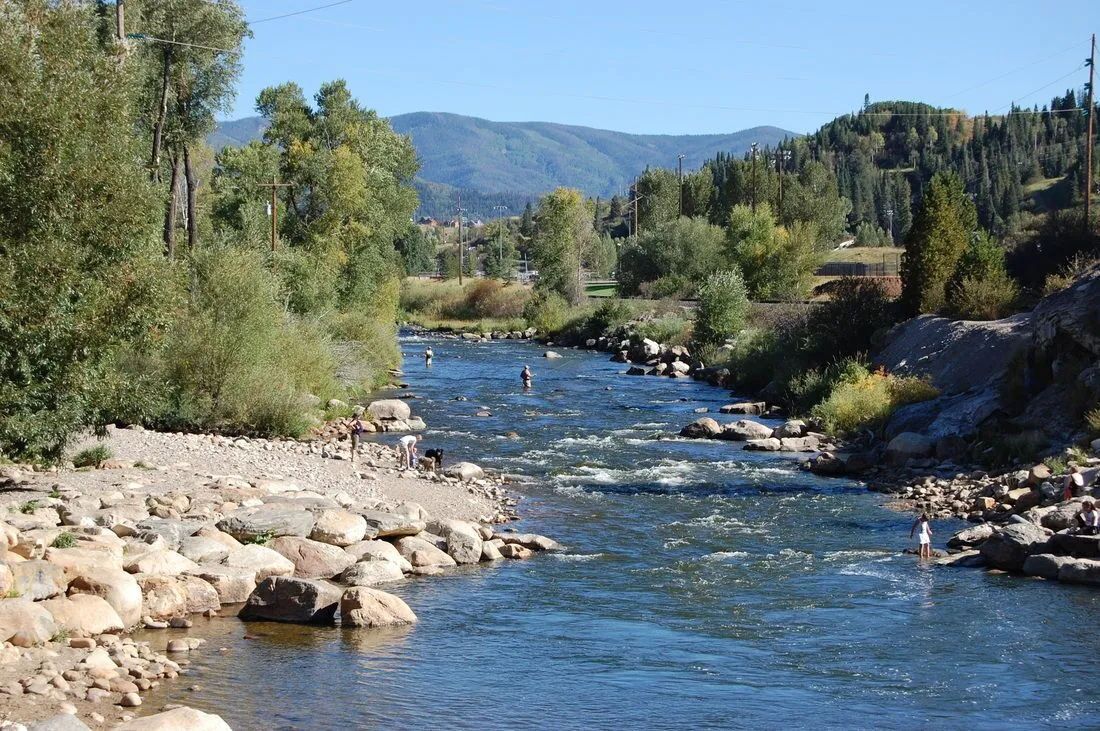 Une rivière bordée de rochers et d’arbres, entourée de collines.