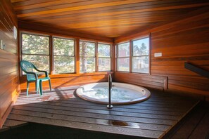 Eine Holzhütte mit Whirlpool, einem Stuhl und großen Fenstern.