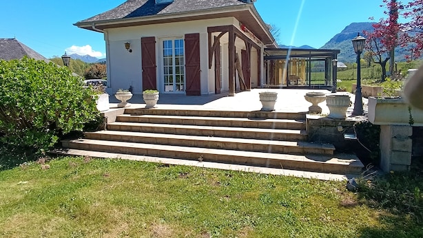 Ein Haus mit geneigtem Dach, einer Veranda mit Stufen und Blick auf Berge im Hintergrund.