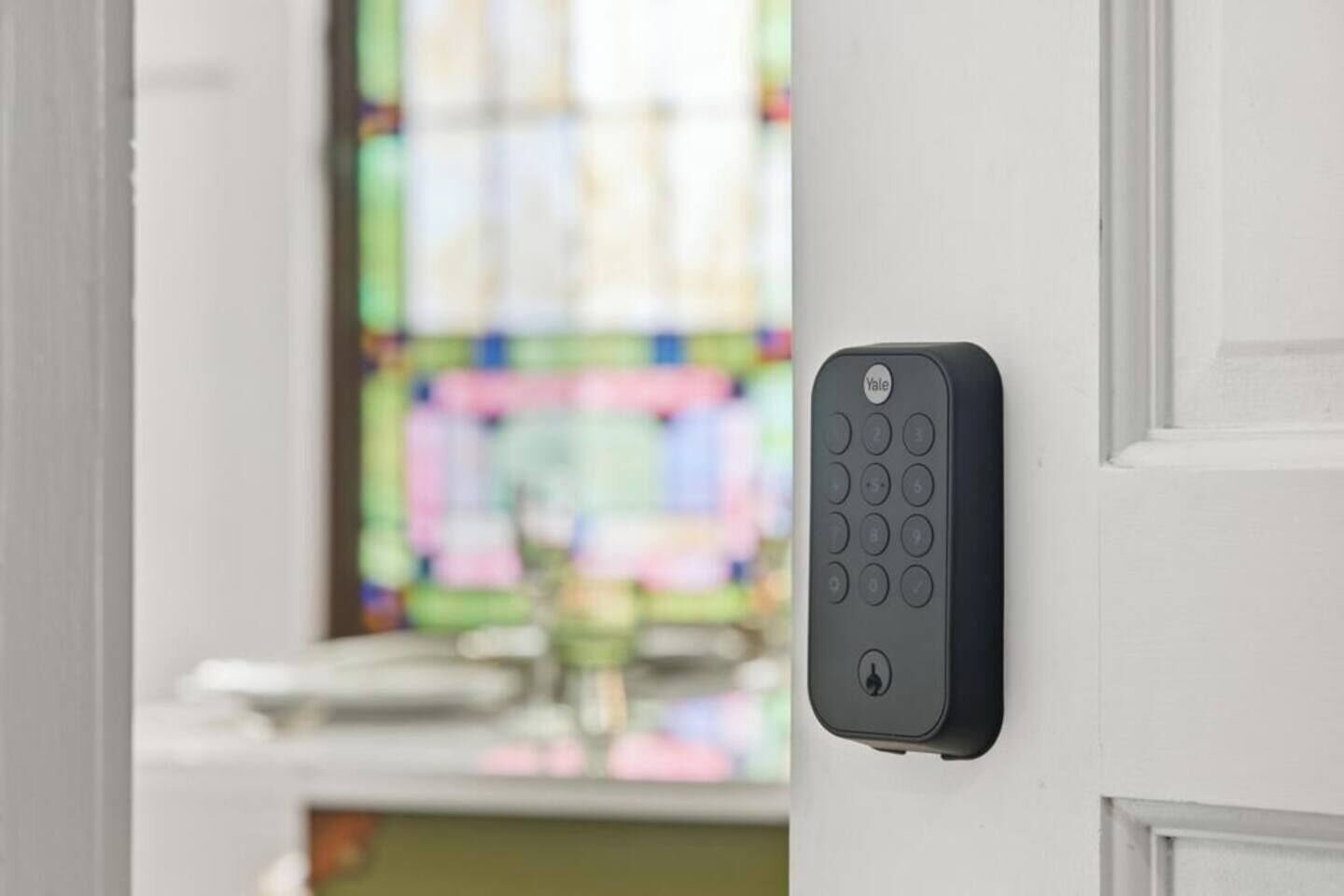 A Yale smart lock installed on a white door, with a blurred stained glass window in the background.