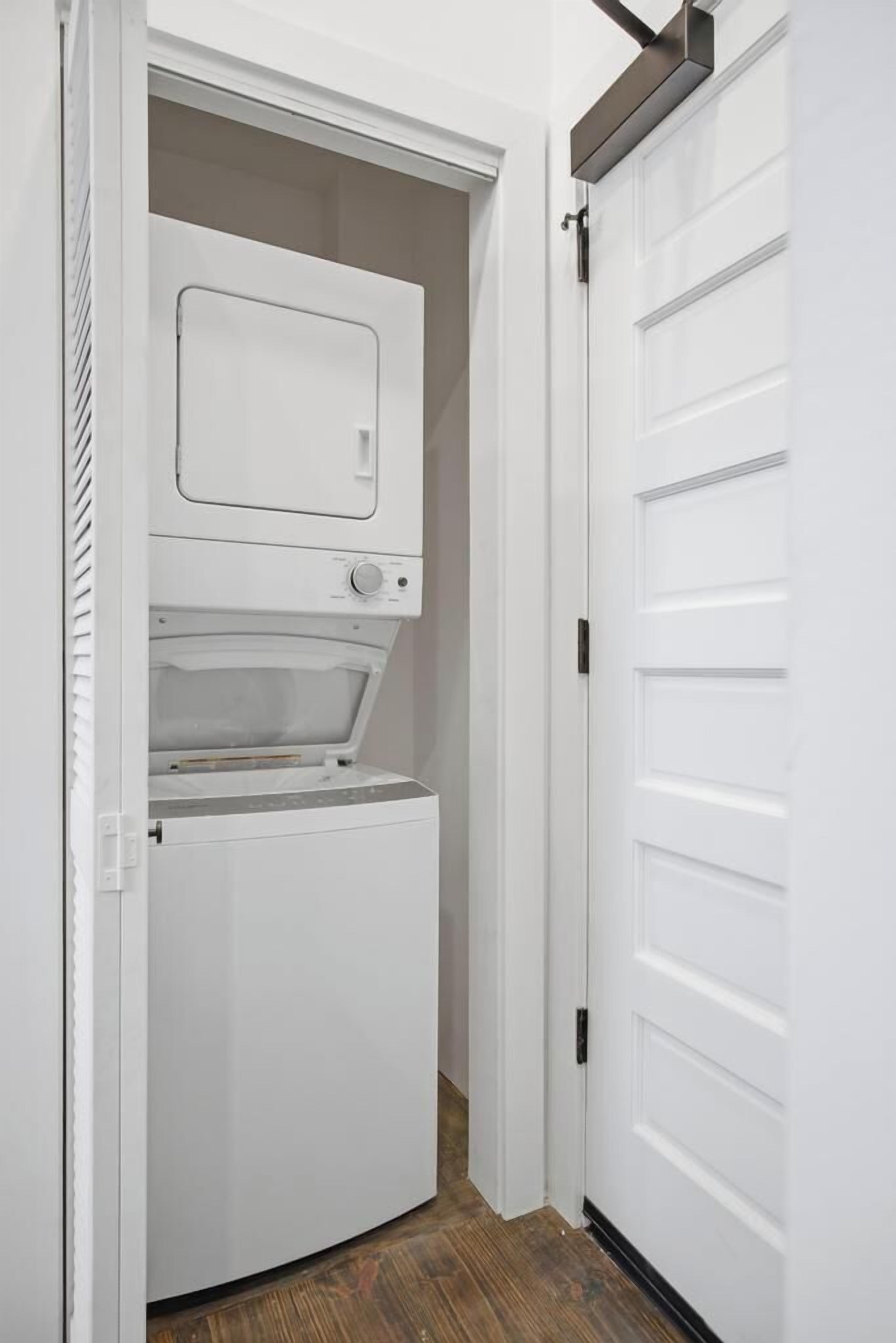 A laundry room with a washer and dryer, a white door, and a wooden floor.