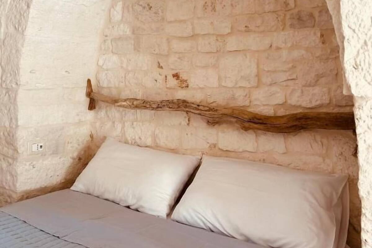 A rustic stone room with a bed under an arched stone ceiling.