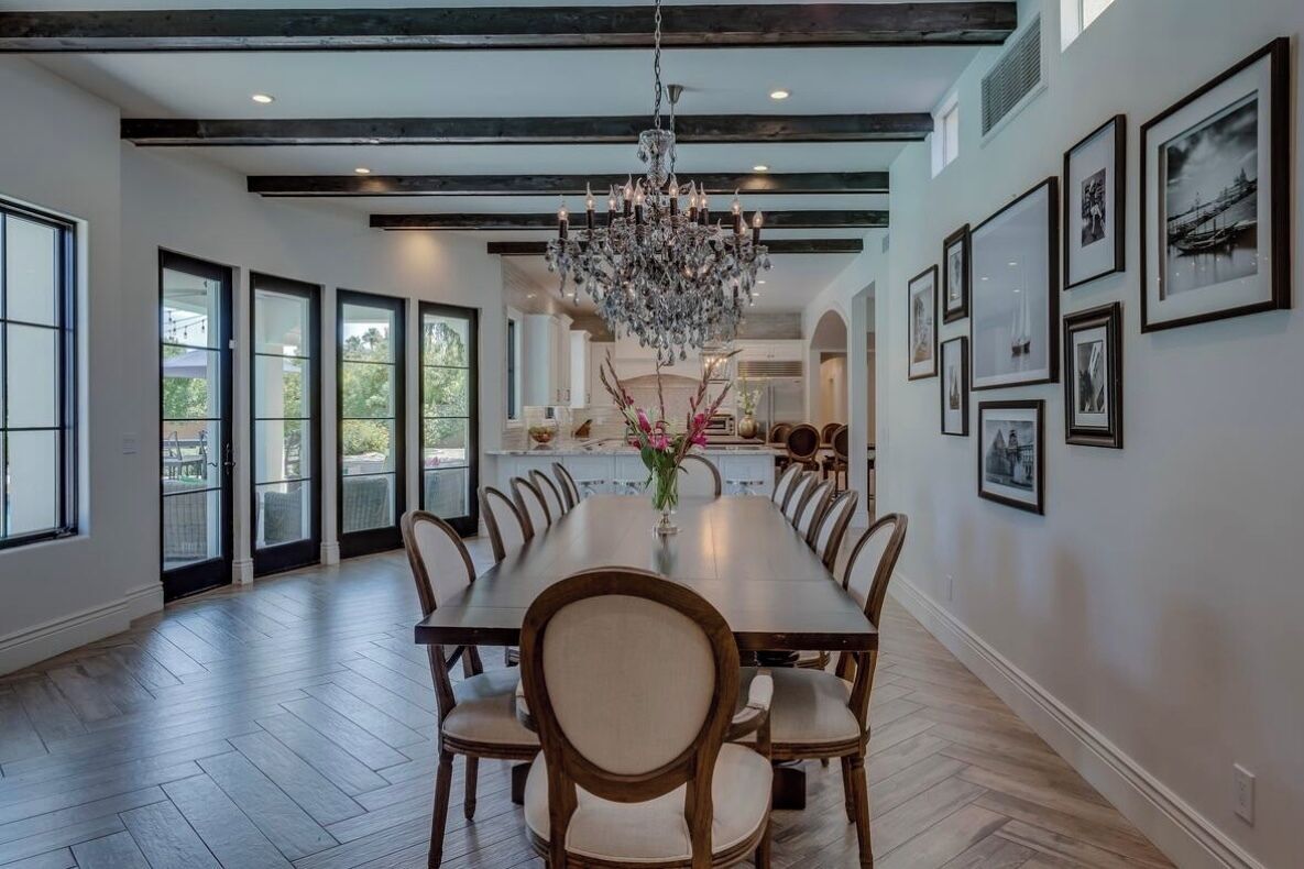 A spacious dining area with a long wooden table, surrounded by chairs, a chandelier, and framed pictures on the walls.