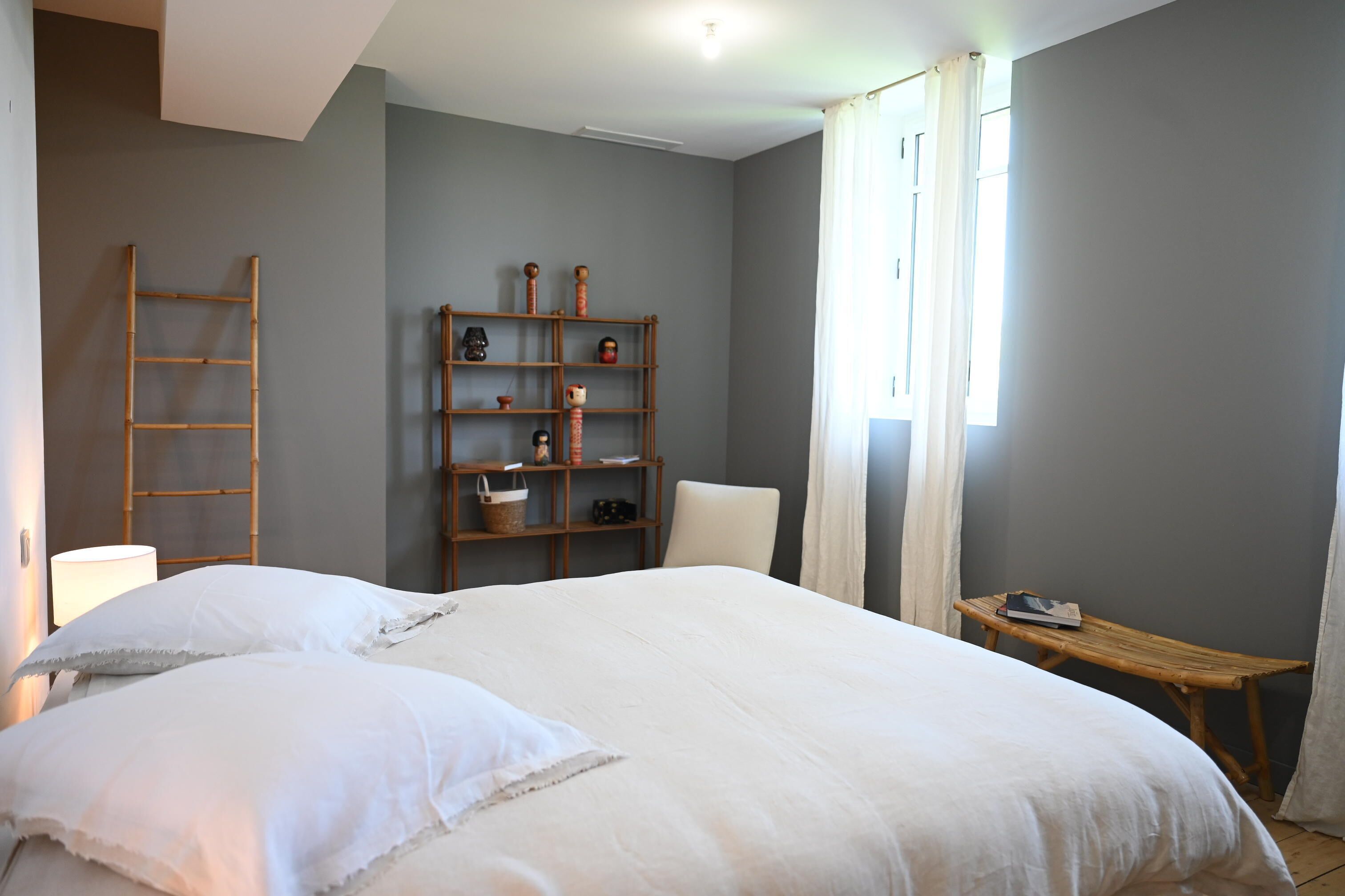 A bedroom with a large bed, a wooden shelf unit, a chair, and a small table.