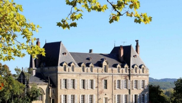 A large, historic stone building with multiple chimneys, a prominent tower, and a symmetrical facade with evenly spaced windows. - Château de Scalibert (Teyssode)