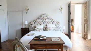 A bedroom with a floral headboard, a wooden bedside table with books, and a white bedspread.
