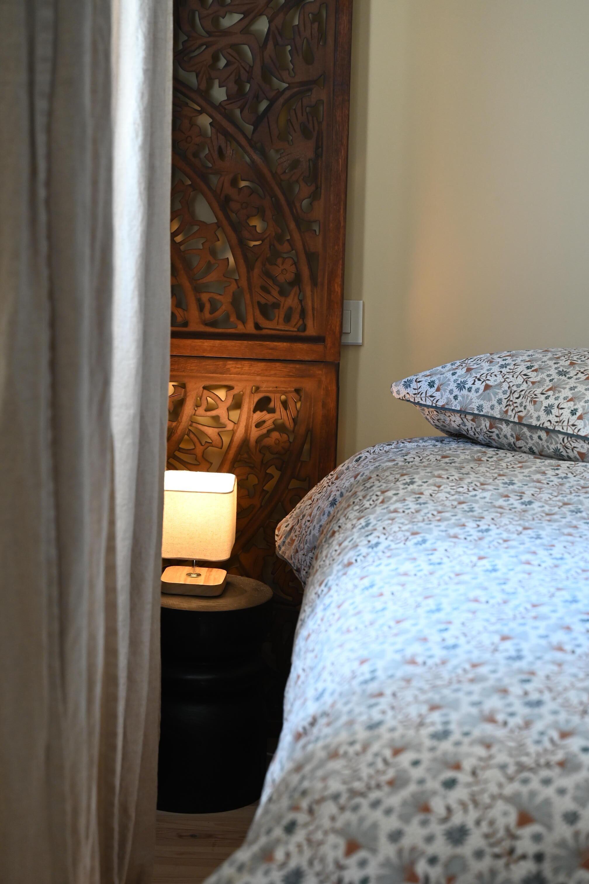 A bedroom with a wooden headboard, a bedside lamp, and a floral-patterned bedspread.