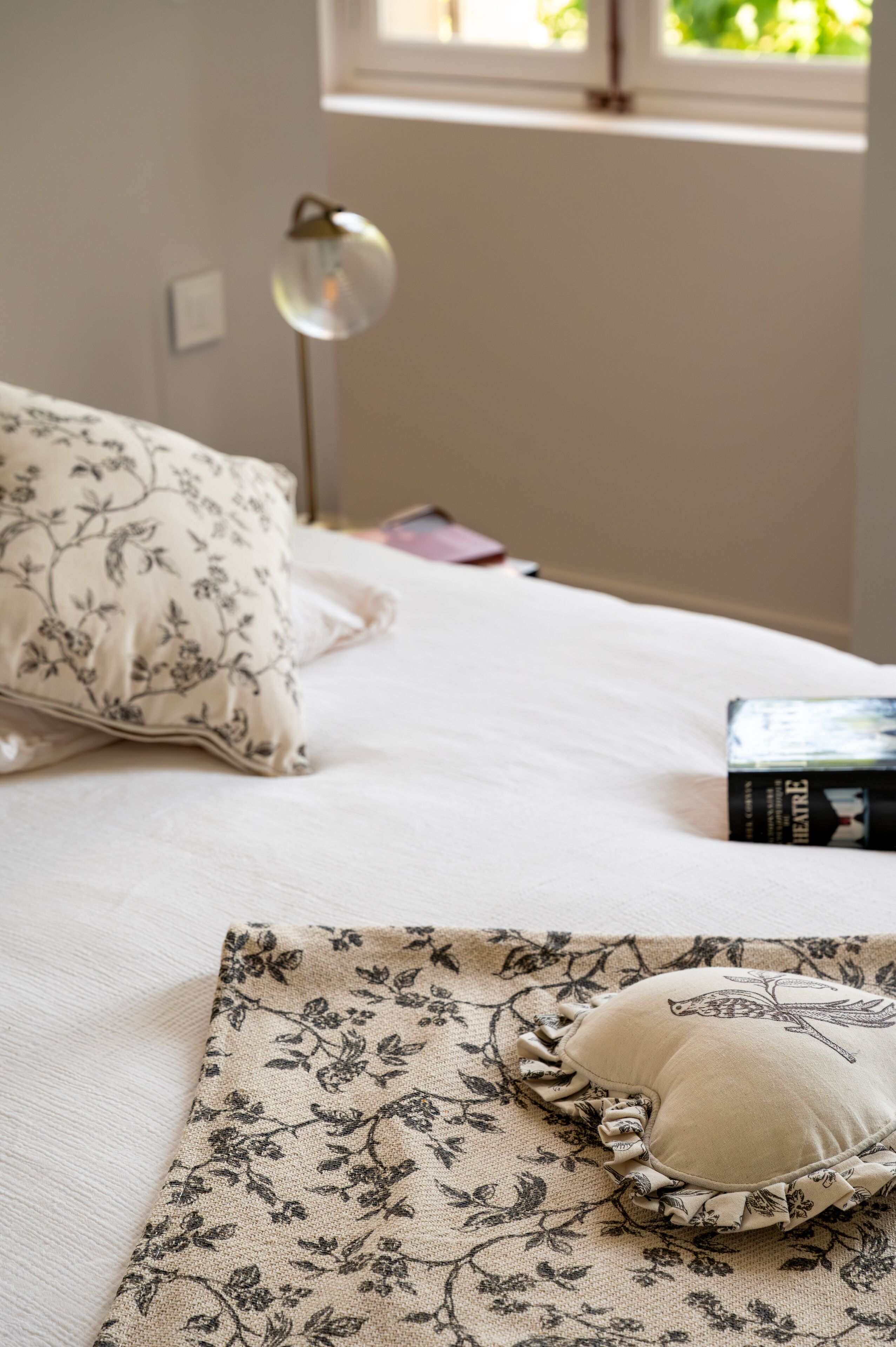 Een opgemaakt bed met bloemenkussens en een boek ernaast.