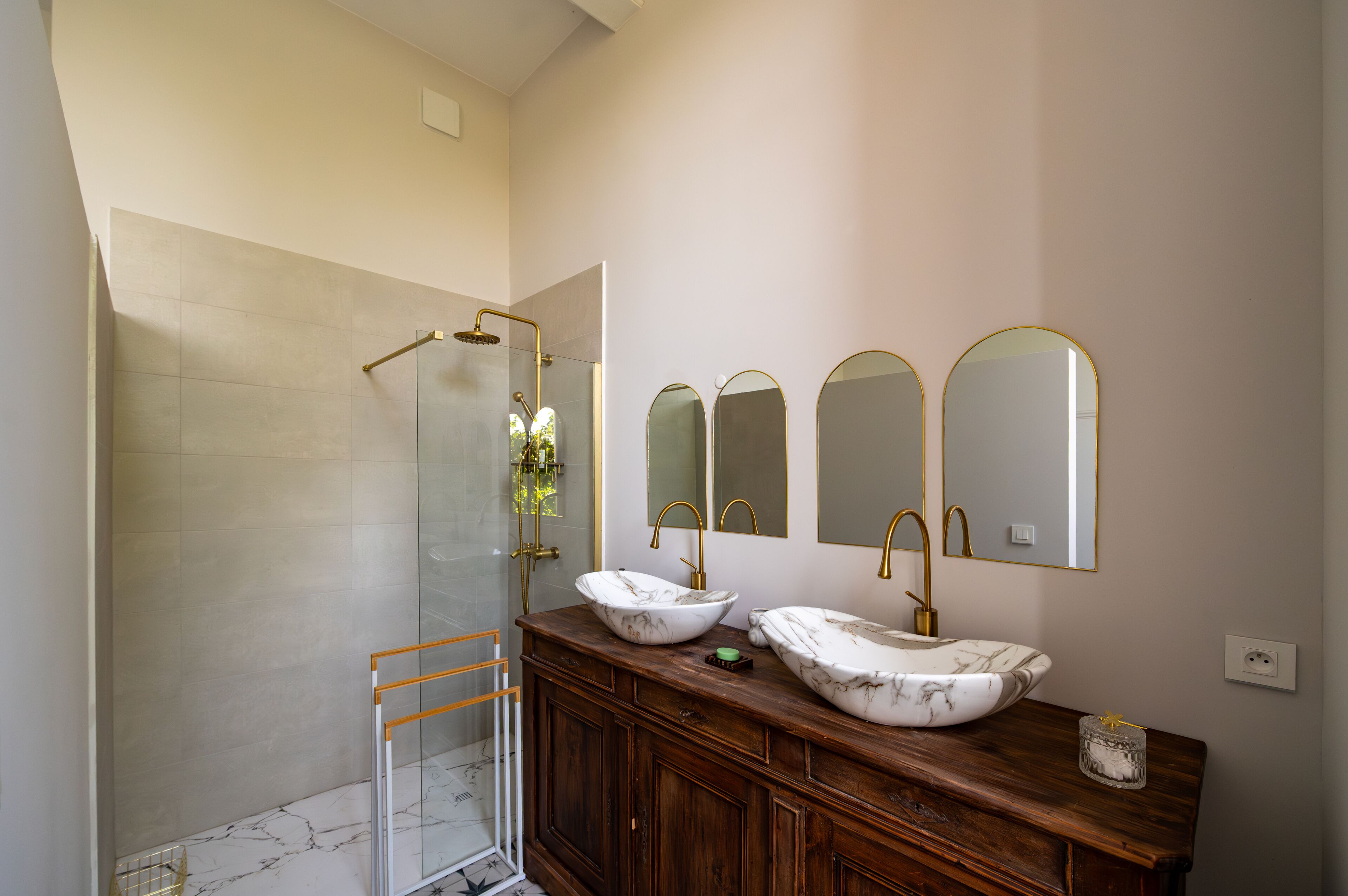 A bathroom with a glass-enclosed shower, two sinks with marble countertops, and three wall-mounted mirrors.