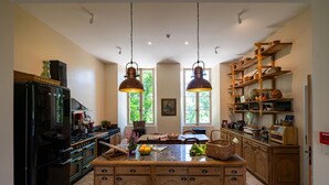 A kitchen with a central island, wooden cabinets, a black refrigerator, and hanging copper pendant lights. - Château de Scalibert (Teyssode)
