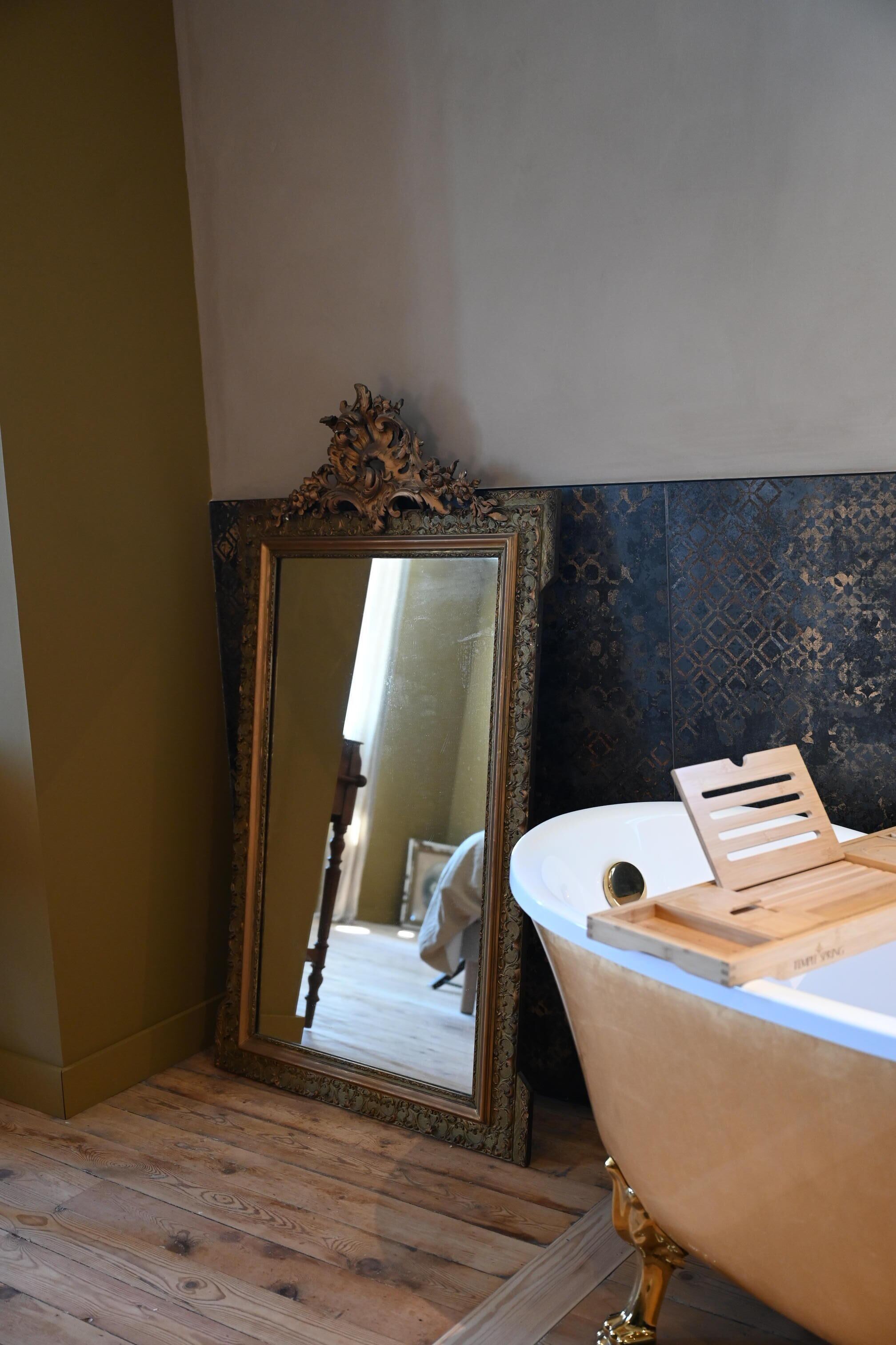A bathroom with a vintage clawfoot bathtub, a large ornate mirror, and a wooden tray on the tub.