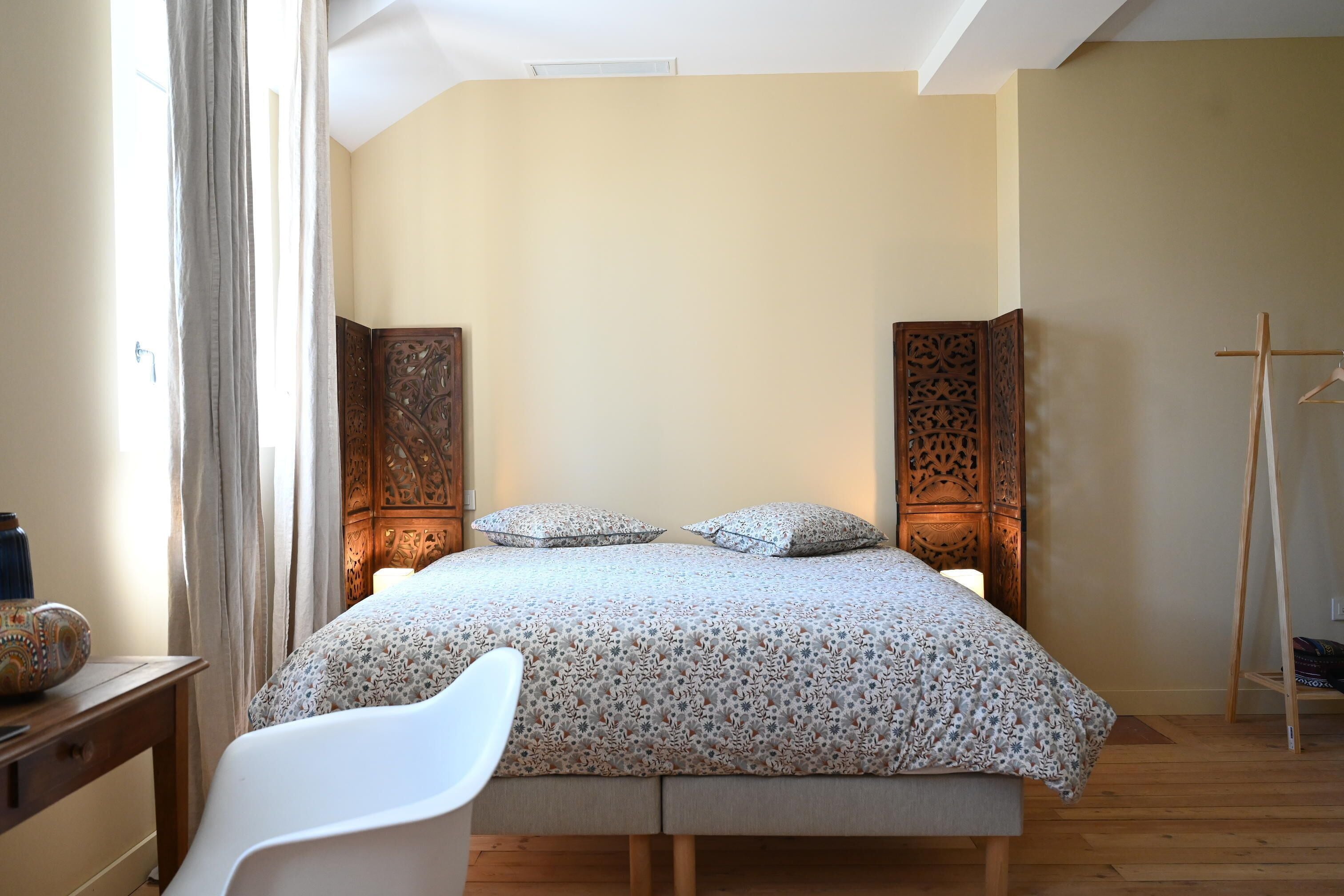 Un dormitorio con una cama, una silla blanca y suelo de madera.
