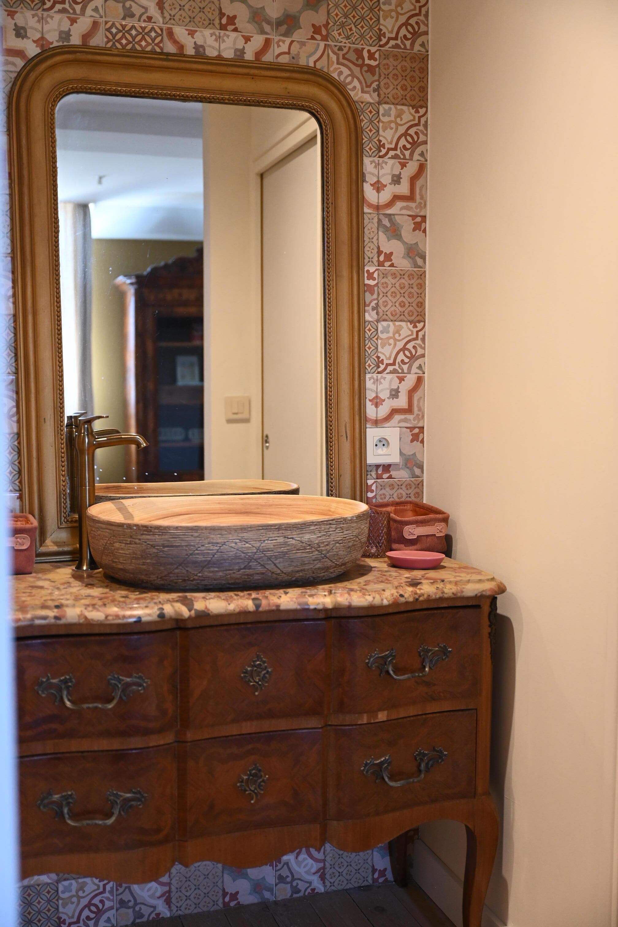 A bathroom vanity with a wooden basin, a large mirror, and a cabinet with drawers.
