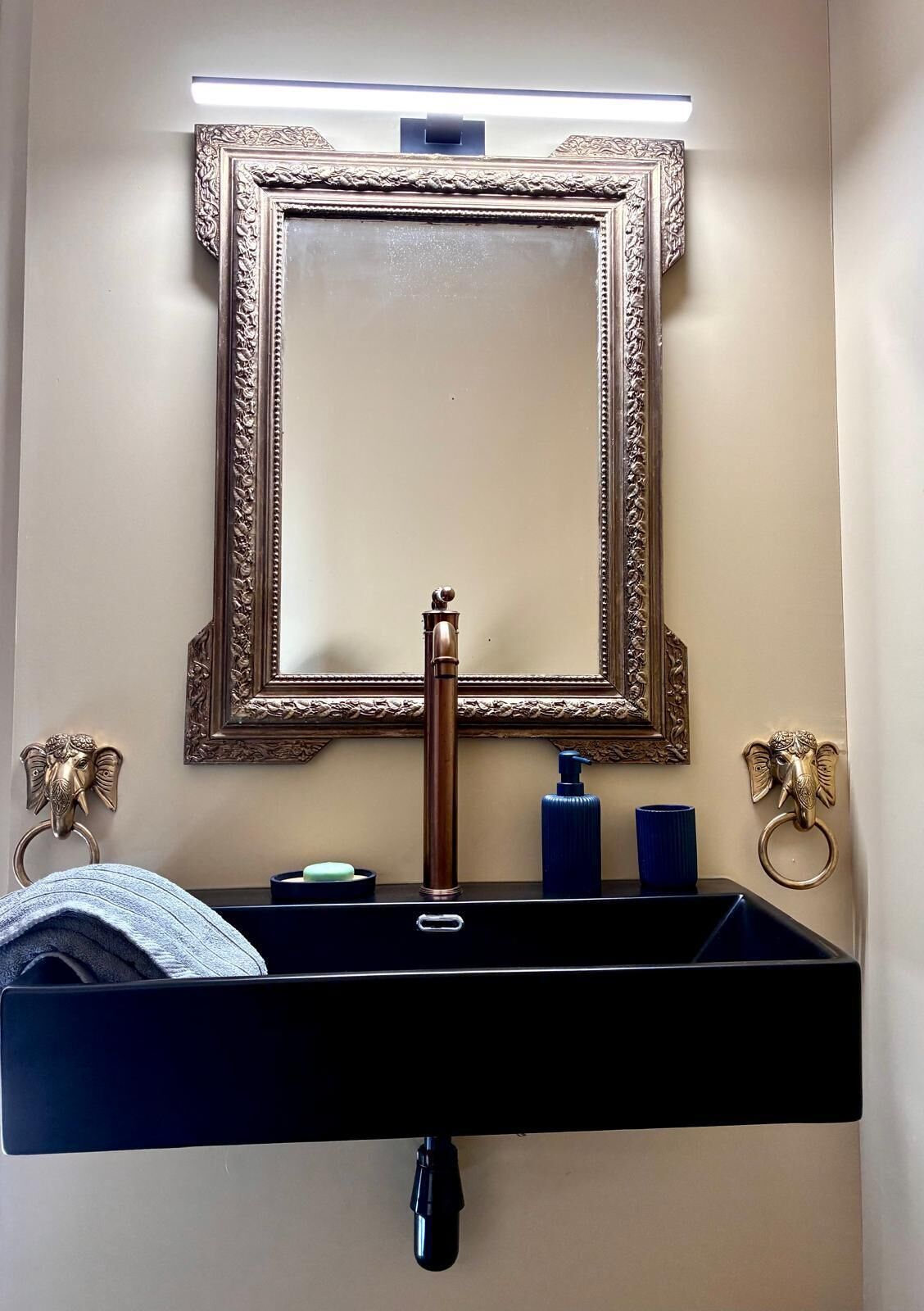 A bathroom with a black sink, a mirror with an ornate frame, and two elephant-shaped towel rings.