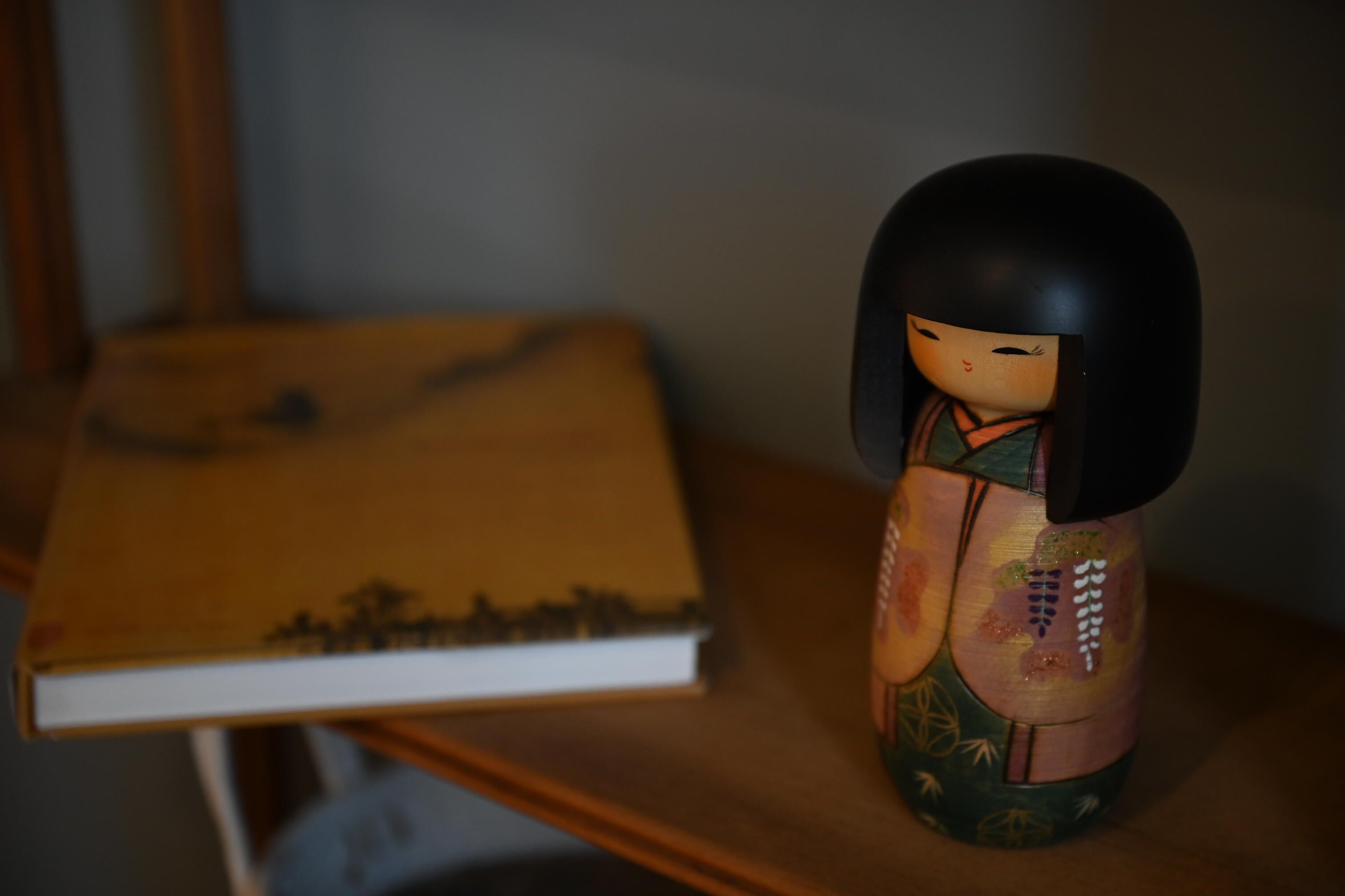A traditional Japanese doll on a wooden table with a book beside it.