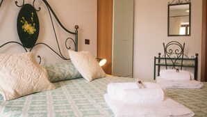 Een opgemaakt bed met kussens, een nachtkastje met een lamp en een spiegel aan de muur.