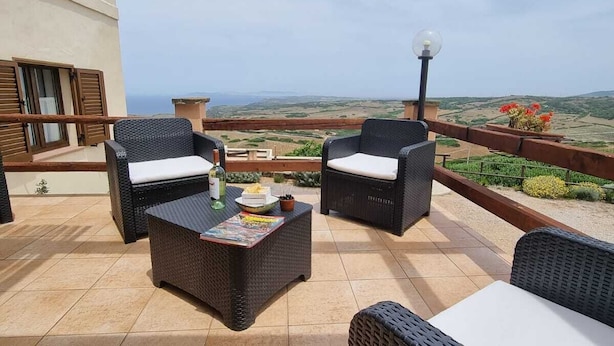 Een terras met rieten meubels, een tafel met een tijdschrift, en uitzicht op het landschap.