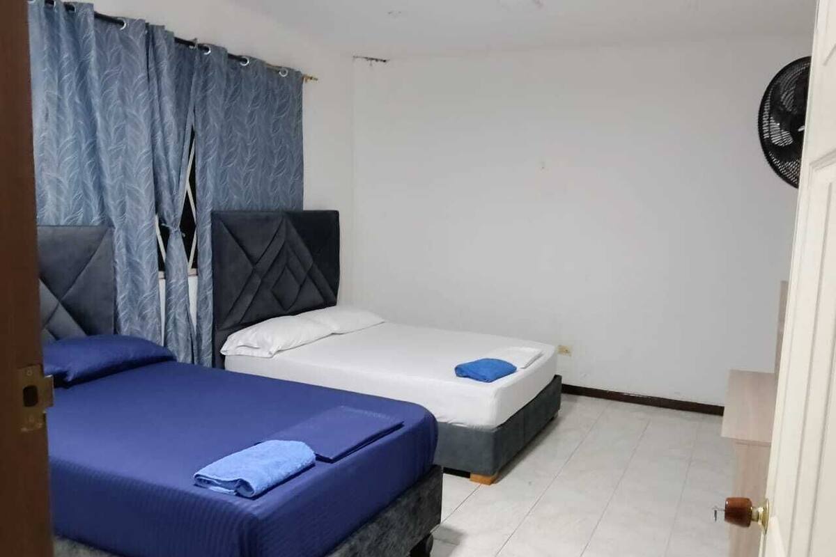 A room with two beds, one with a blue bedspread and the other with a white bedspread.