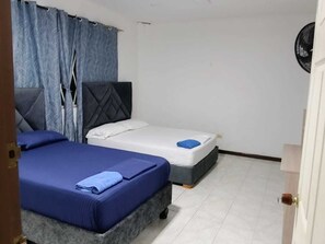 A room with two beds, one with a blue bedspread and the other with a white bedspread.