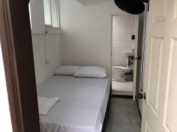 A small, clean room with a single bed, a window, a toilet, and a sink.