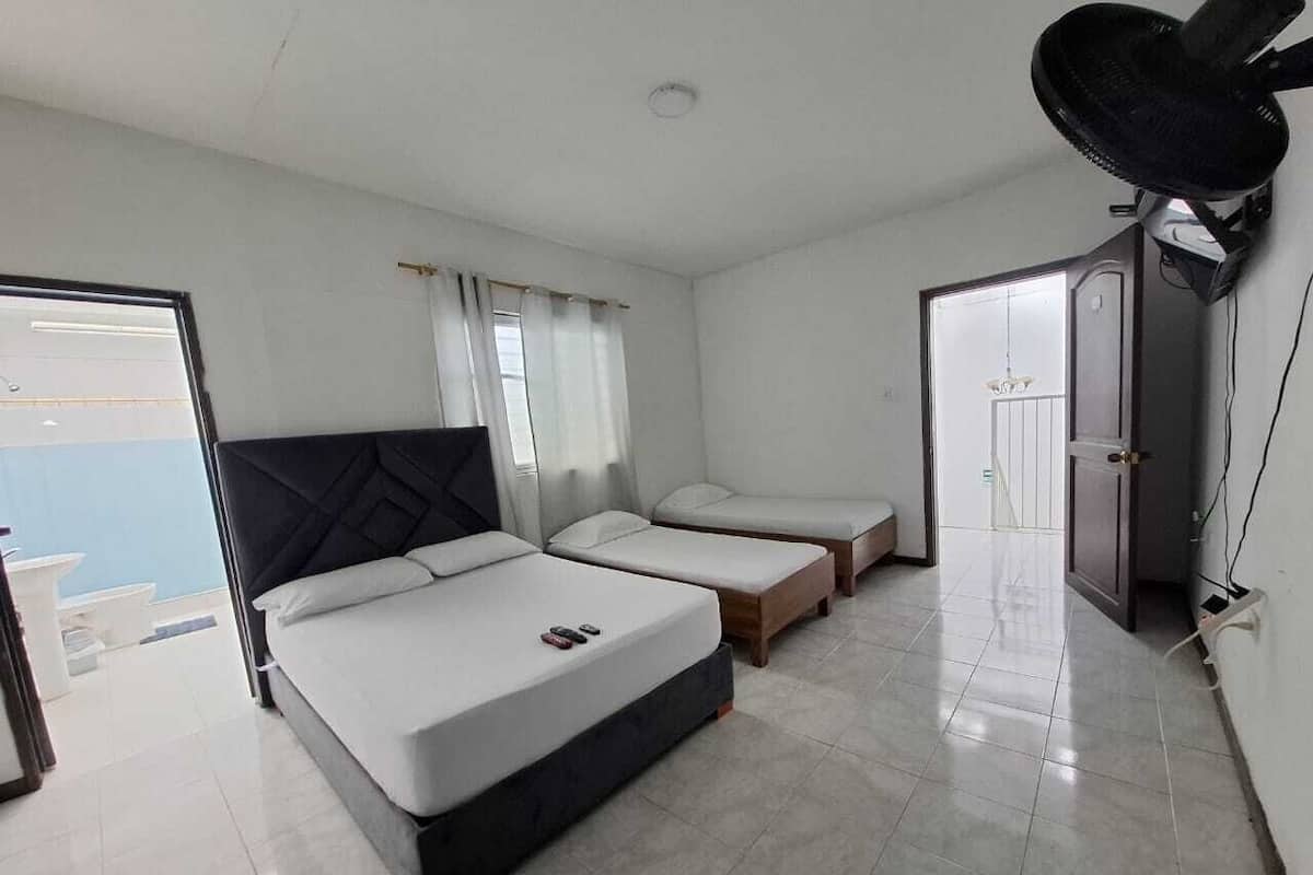 A bedroom with a large bed, two smaller beds, a ceiling fan, and a view of the outside.