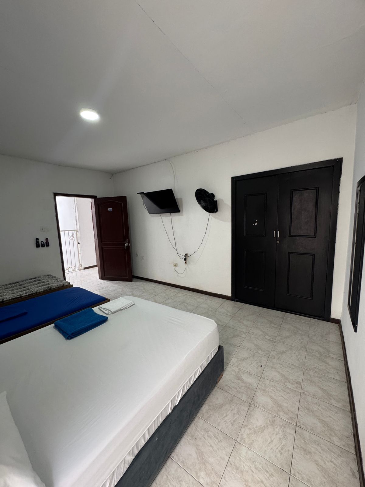 Un dormitorio con cama, armario, puerta y ventilador de pared.