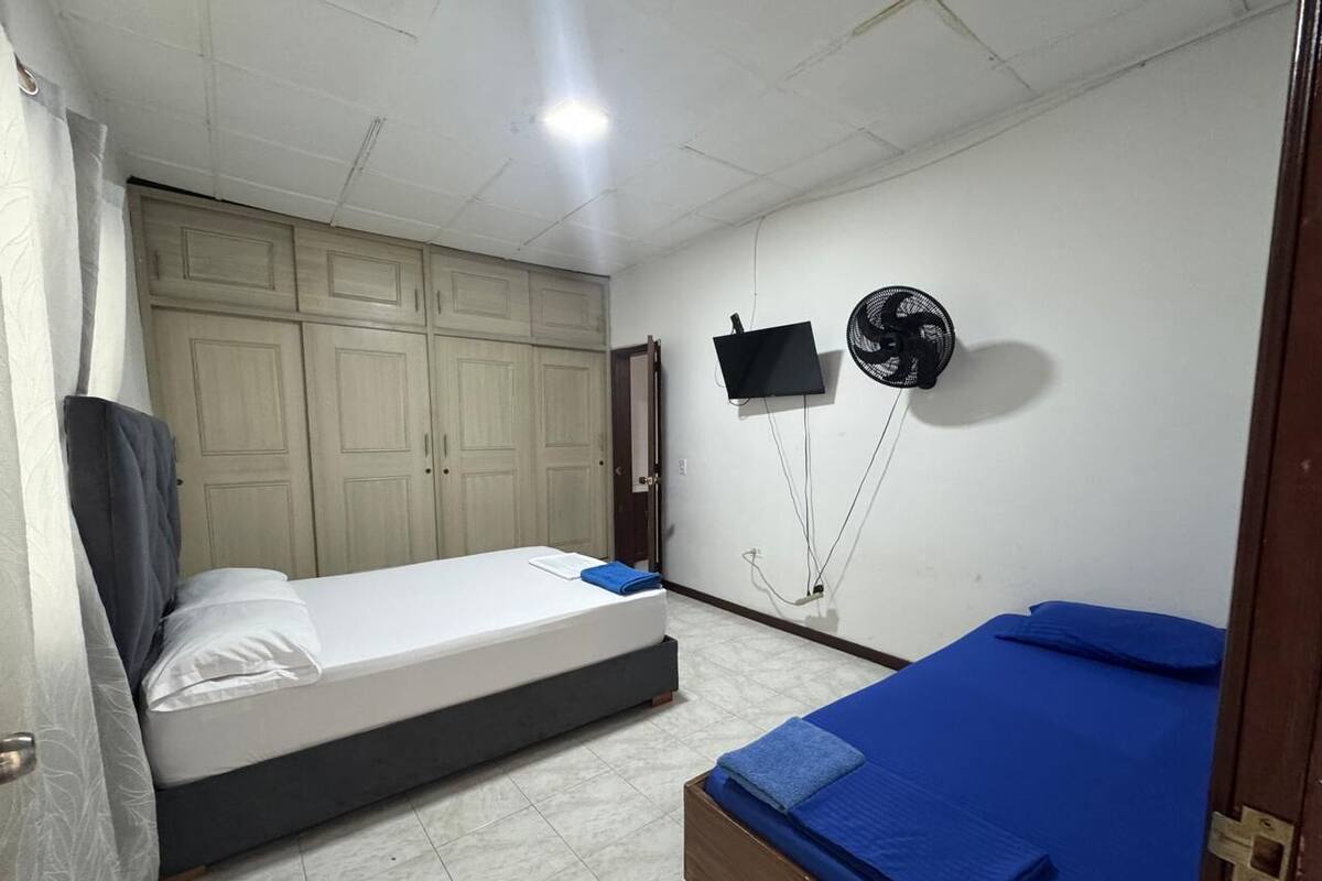 A room with two beds, a wardrobe, a TV, and a fan.