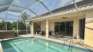 A swimming pool with a covered patio area, outdoor furniture, and a sliding glass door leading to a covered patio. - Resort-Style 3BR Home with Pool & Hot Tub in a Golf Course Community (Bonita Springs)
