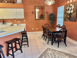 A dining area with a wooden table and chairs, a white countertop with a sink, and a decorative rug. - Resort-Style 3BR Home with Pool & Hot Tub in a Golf Course Community (Bonita Springs)