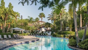 Une piscine entourée de palmiers et de verdure, avec des chaises longues et des parasols.