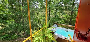 Een hottub in een bebost gebied met een houten terras en gele veiligheidsreilingen.