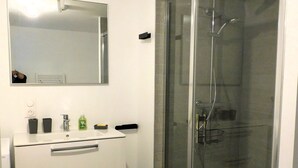 Un baño con ducha envuelta en vidrio, un lavabo blanco con espejo y una pequeña alfombra naranja en el suelo.