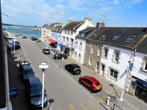 A street view with parked cars, buildings, and a clear sky. - Charming apartment💕 Near the ocean🏄‍♀️ and sandy beaches🏖️ Relaxation guaranteed! (Loctudy)