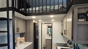 A compact kitchen with a central island, wooden flooring, and a mezzanine with a bed. - And.N Lodging  (Casco)