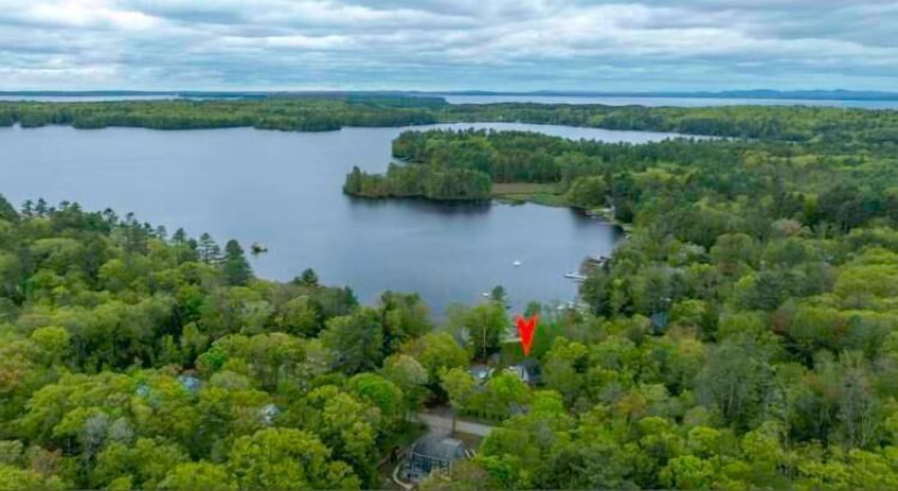 An aerial view of a lake surrounded by dense forest, with a small building and dock visible in the foreground.
