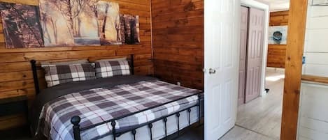 Een slaapkamer met een bed, houten wanden, een plafondventilator en een deur naar een andere kamer.