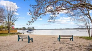 A sandy beach with two green benches facing a calm lake. - And.N Lodging  (Casco)