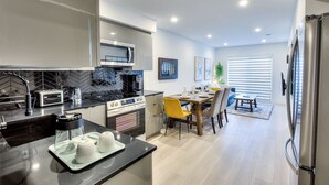 A modern kitchen with a microwave, toaster, and stove. There is a dining area with a table and chairs. - Elegant 2BR Suite Close to Transit (Montréal)