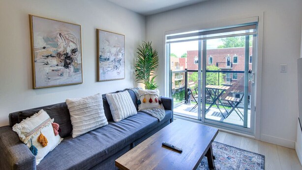 A modern living room with a grey sofa, a coffee table, and two abstract paintings on the wall. - Elegant 2BR Suite Close to Transit (Montréal)
