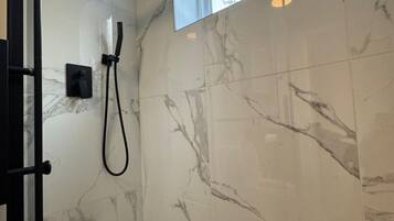 A bathroom with a shower, a window, and a marble wall.