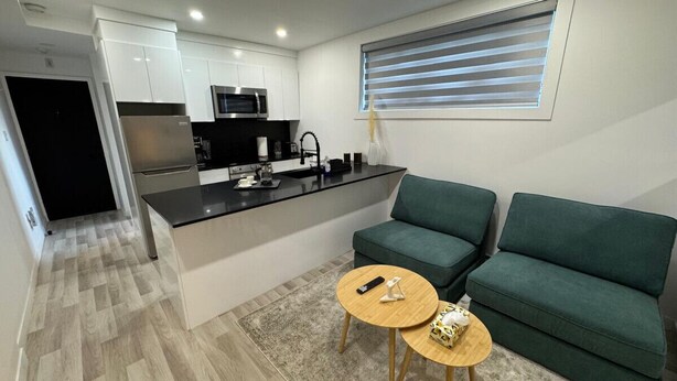 A compact living space with a kitchenette, a green sofa, and two small round tables. - NDG Treasure in Montreal! Value & Travel Adventure (Montréal)