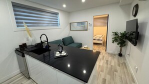 A modern kitchen with a black countertop, white cabinets, and a small dining area with a green sofa. - NDG Treasure in Montreal! Value & Travel Adventure (Montréal)