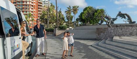 A paved walkway with a stone wall and palm trees, leading to a building with balconies.